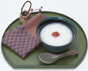 plateau rond sur lequel est posé une cuillère, une serviette et un bol rempli de riz sur lequel est posé une prune umeboshi