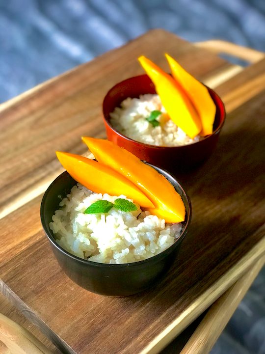 deux bols de riz au lait de coco avec mangue sur une planche en bois