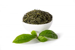 feuilles de thé vert dans un bol blanc et feuilles de thé vert fraîches