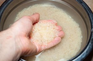 main qui lave du riz dans un récipient