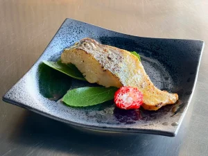 Poisson grillé japonais sur une assiette en céramique noire, avec décoration