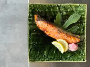 Saumon grillé mariné sur une assiette en céramique verte et deux tranches de citron