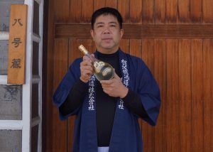 producteur de saké japonais avec une bouteille à la main devant un mur de bois