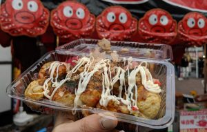 une barquette de takoyaki tenue dans une main dans la rue