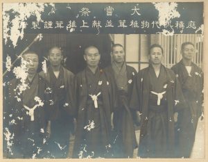 Photo argetnique de 6 hommes en kimonos japonais qui se tiennent debout sous une banderole 