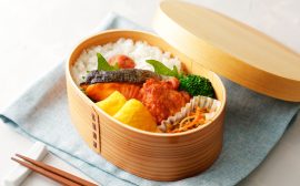 Focus sur une boîte de bento japonais en bois avec du riz des légumes et du saumon grillé sur une serviette bleu