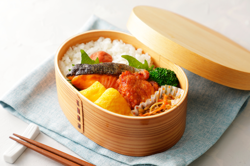 Focus sur une boîte de bento japonais en bois avec du riz des légumes et du saumon grillé sur une serviette bleu