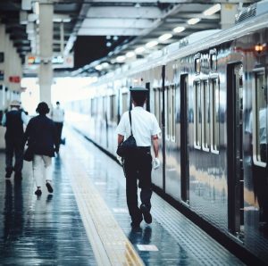 Train en gare avec un contrôleur japonais en chemise blanche et pantalon de travail, qui marche sur le quai