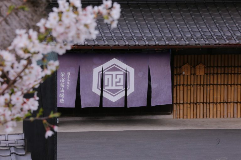 Photo de la devanture d'une entreprise japonaise avec un rideau noren violet et un logo blanc