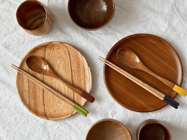 Tasses, assiettes, baguettes et cuillères en bois laqué sur une nappe blanche