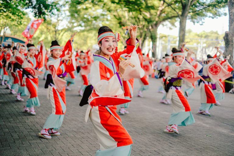 Femmes asiatiques en costumes colorés qui avancent et dansent en groupe dans la rue, avec du maquillage et des tenues traditionnelles